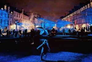 Europe Évènement - Rencontre des étoiles - Photo du centre-ville de Caen avec des faisceaux laser bleus et une structure en forme d'étoile au centre