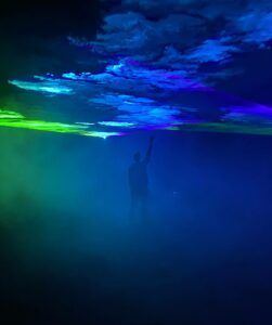 Europe Évènement - Photo of a man raising his hand to touch the blue and green smoke projection